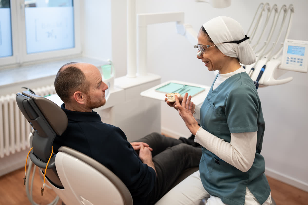 Eine Zahnärztin erklärt einem Patienten den geplanten Zahnersatz an einem Modell